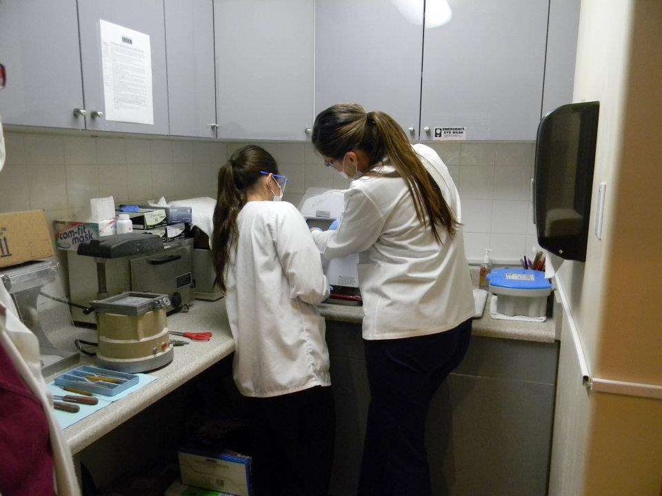 Two individuals wearing white lab coats are working in a kitchen with various scientific equipment, such as beakers and test tubes, on a countertop.
