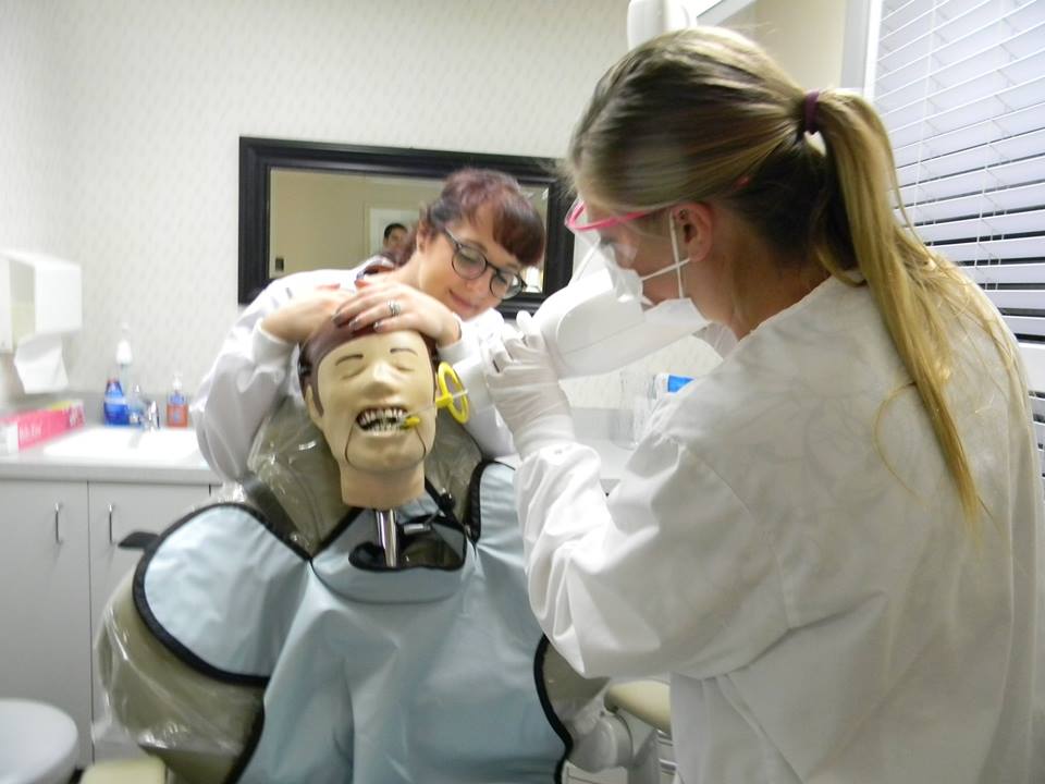 In the image, a person is seated in a dental chair with a dental mask on their face, receiving attention from a dental professional who is adjusting or checking the mask while other dental equipment is visible around them.
