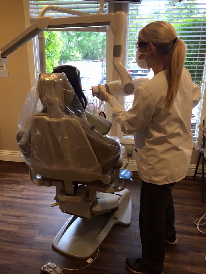 A hairstylist, wearing a white coat and a face mask, is working on a hair salon chair with a clear plastic covering, adjusting the chair s height using a lever.