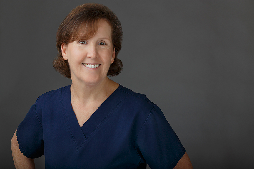 The image shows a woman wearing scrubs and standing with her arms crossed.